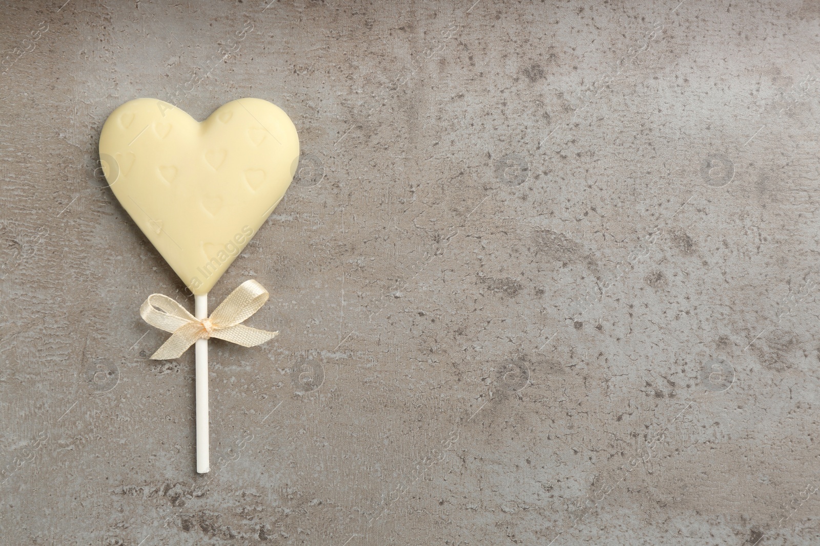 Photo of Chocolate heart shaped lollipop on grey table, top view. Space for text