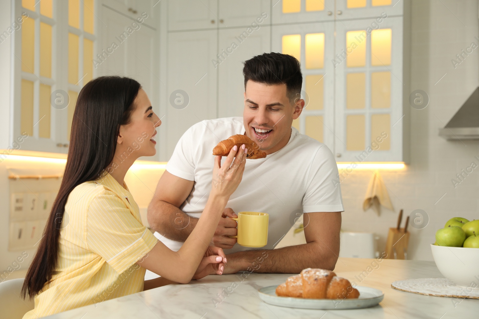 Photo of Happy couple wearing pyjamas during breakfast at table in kitchen