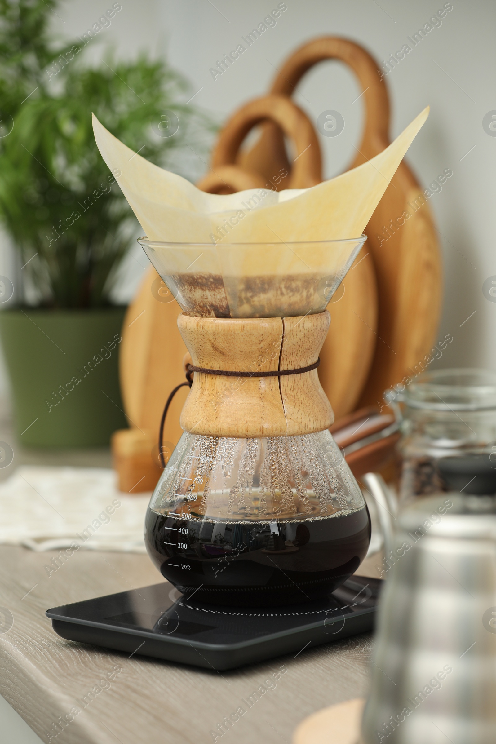 Photo of Glass chemex coffeemaker with paper filter and coffee on wooden countertop in kitchen