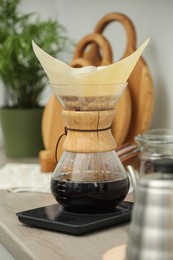 Photo of Glass chemex coffeemaker with paper filter and coffee on wooden countertop in kitchen