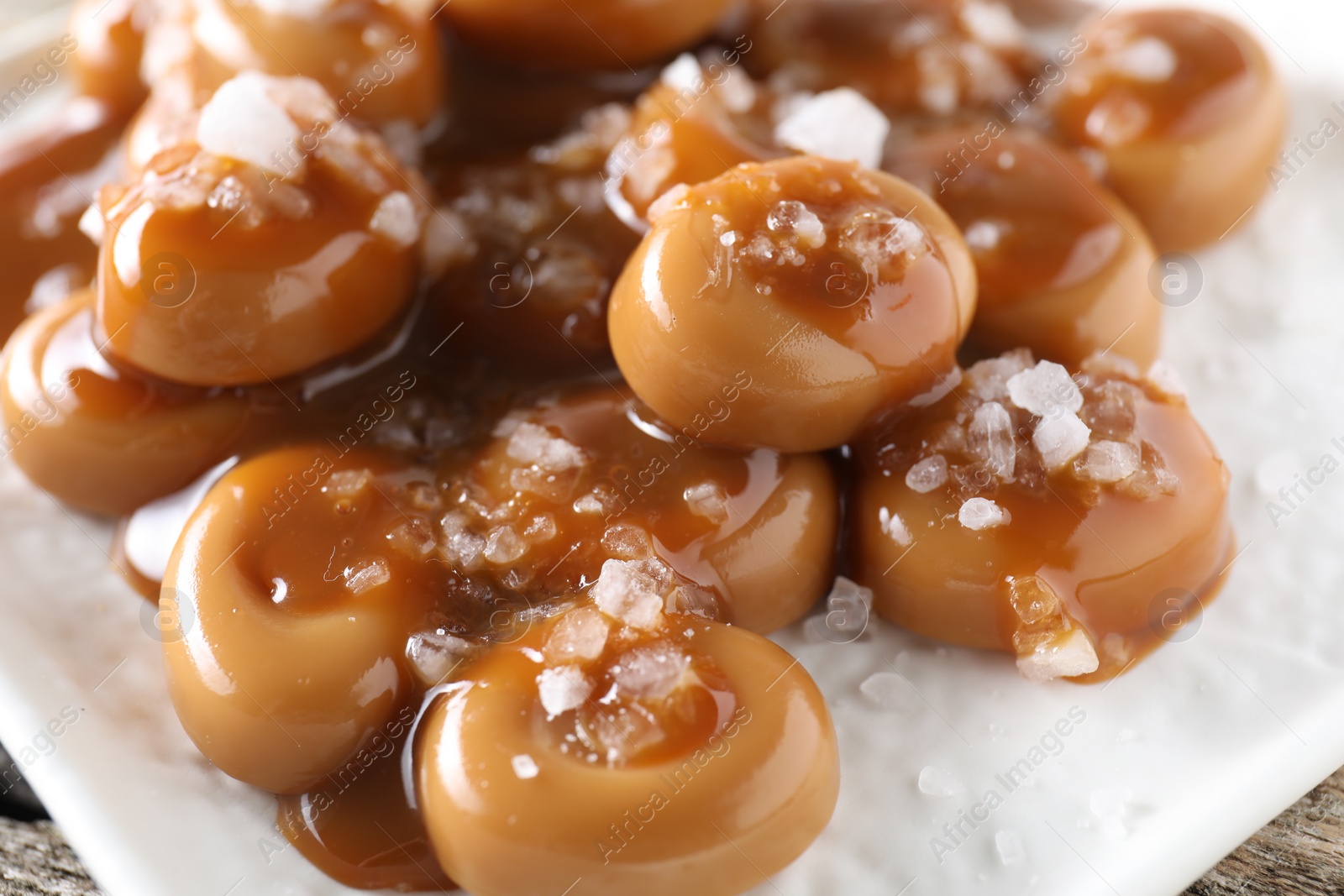 Photo of Tasty candies, caramel sauce and salt on wooden table, closeup