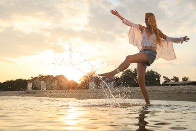 Photo of Beautiful young woman playing with water on sea beach at sunset, space for text