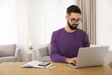 Handsome young man working with laptop at table in home office