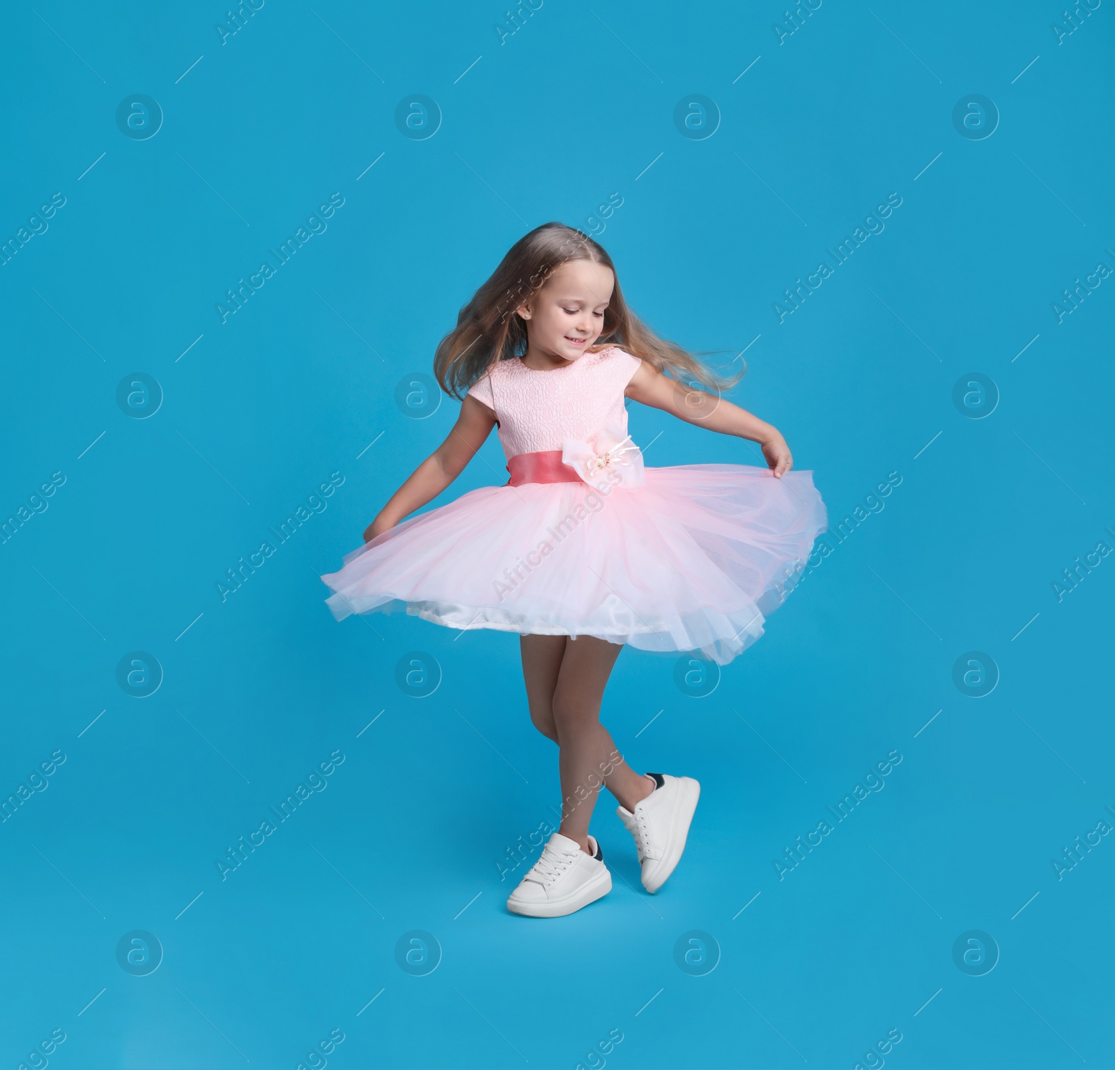 Photo of Cute little girl in beautiful dress dancing on light blue background