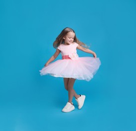 Photo of Cute little girl in beautiful dress dancing on light blue background