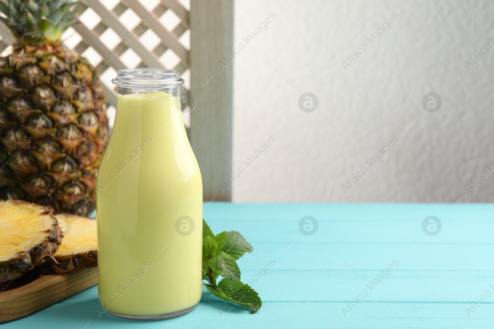 Photo of Tasty pineapple smoothie in bottle, mint and fruit on light blue wooden table. Space for text