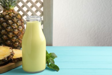 Photo of Tasty pineapple smoothie in bottle, mint and fruit on light blue wooden table. Space for text