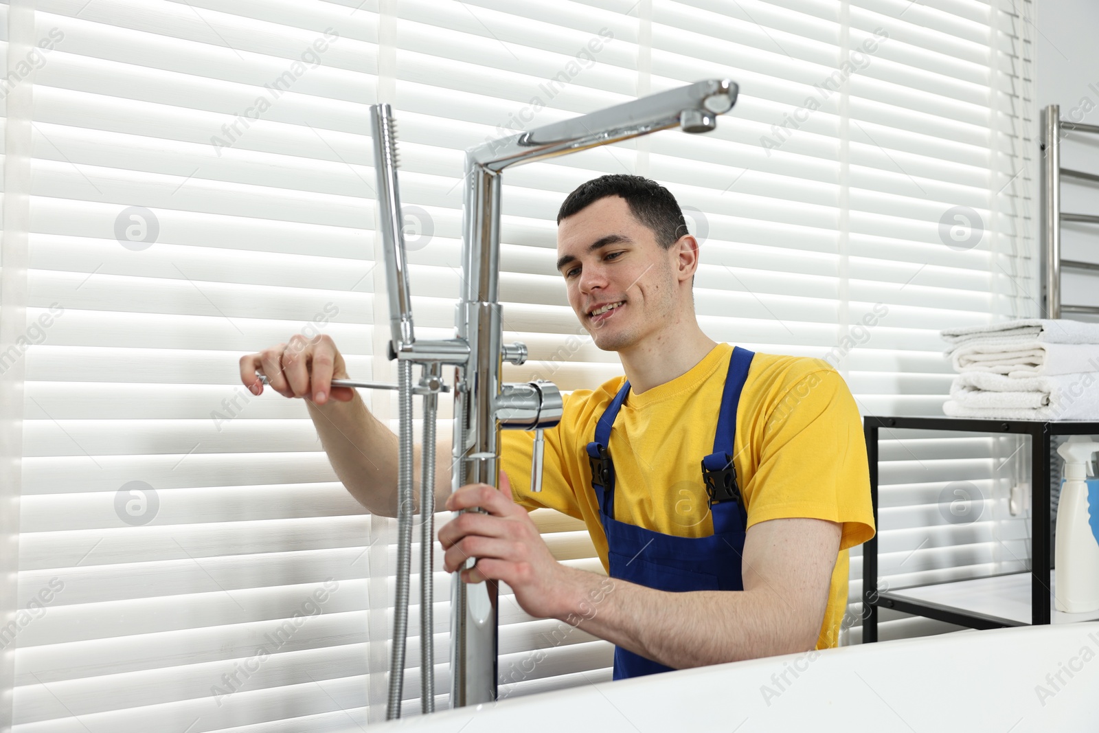 Photo of Smiling plumber repairing faucet with spanner in bathroom