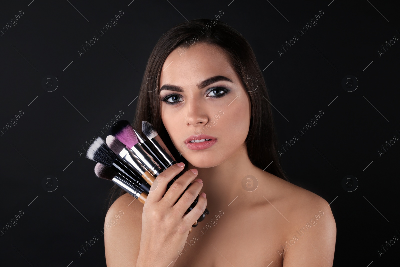 Photo of Portrait of beautiful woman with makeup brushes on dark background