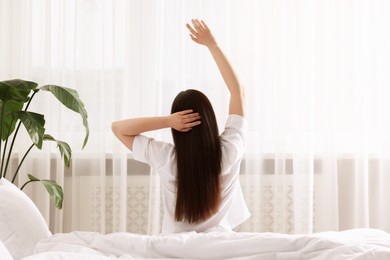 Photo of Woman stretching on bed at home, back view. Lazy morning