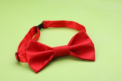 Stylish red bow tie on light green background, closeup