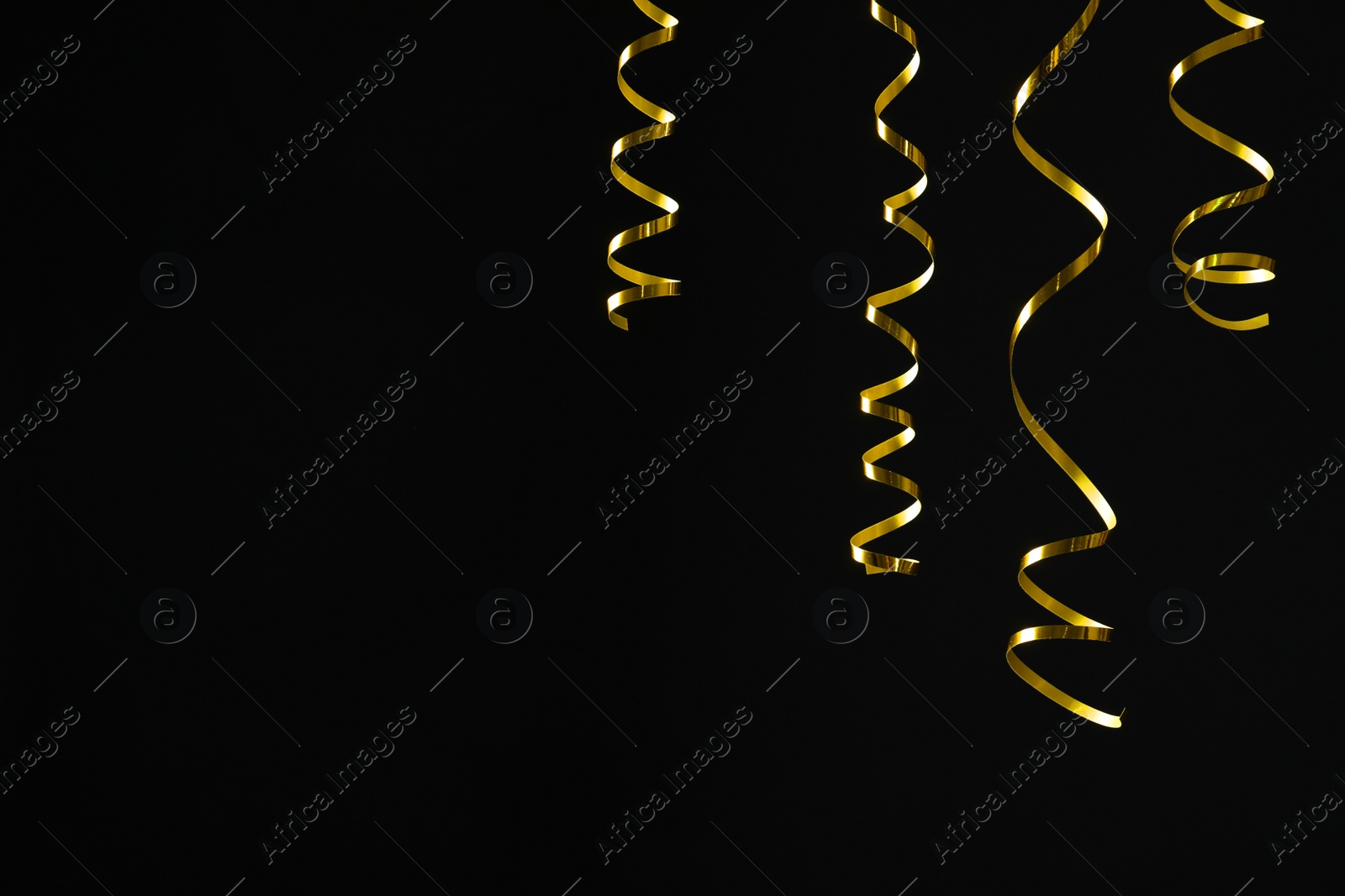 Photo of Shiny golden serpentine streamers on black background. Space for text