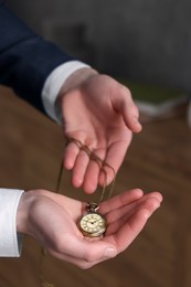 Man holding chain with elegant pocket watch on blurred background, closeup