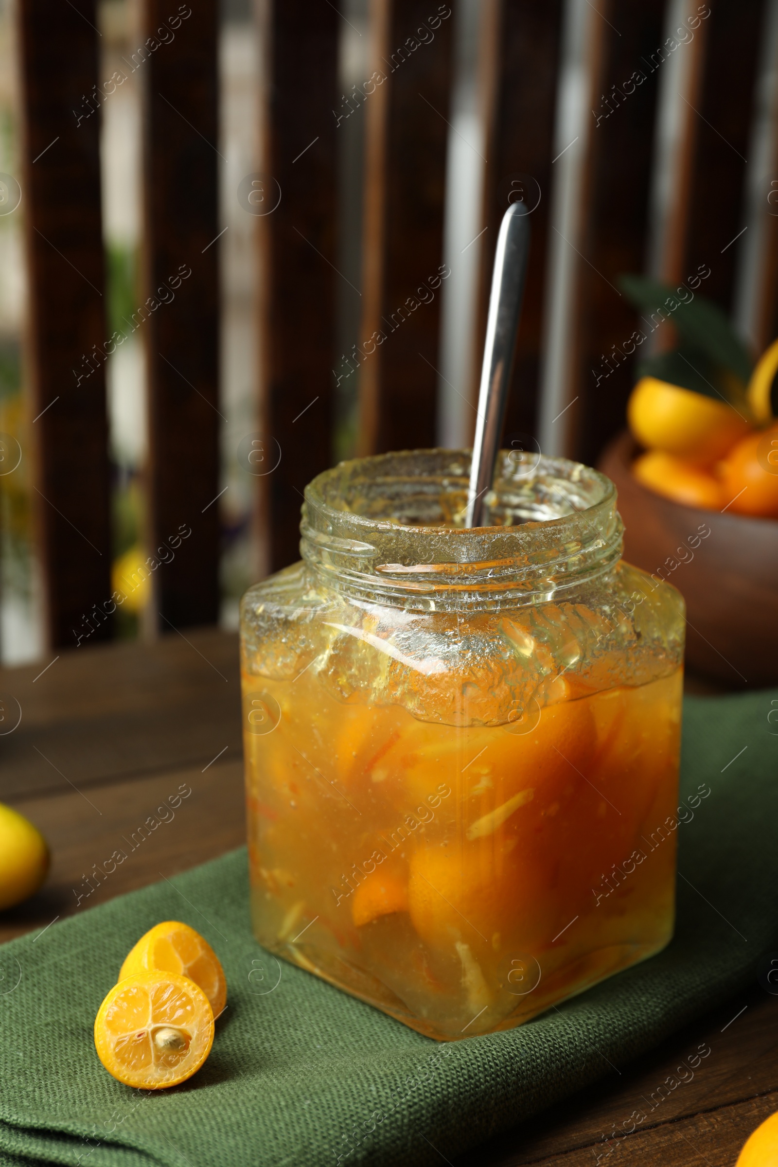 Photo of Delicious kumquat jam in jar and fresh fruits on wooden table