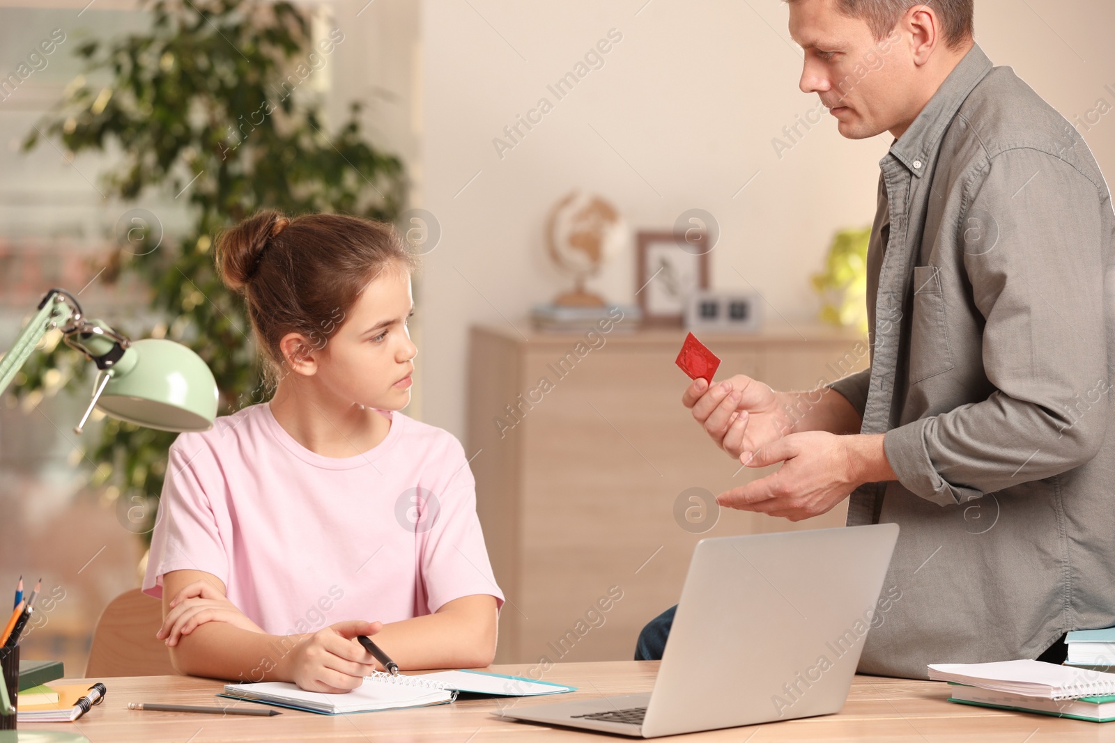 Photo of Father talking with his teenage daughter about contraception while she doing homework at home. Sex education concept