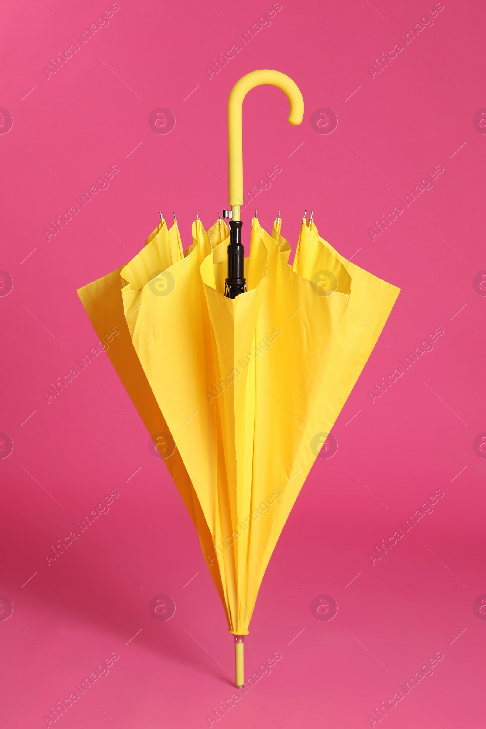 Photo of Stylish closed yellow umbrella on pink background