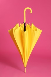 Stylish closed yellow umbrella on pink background
