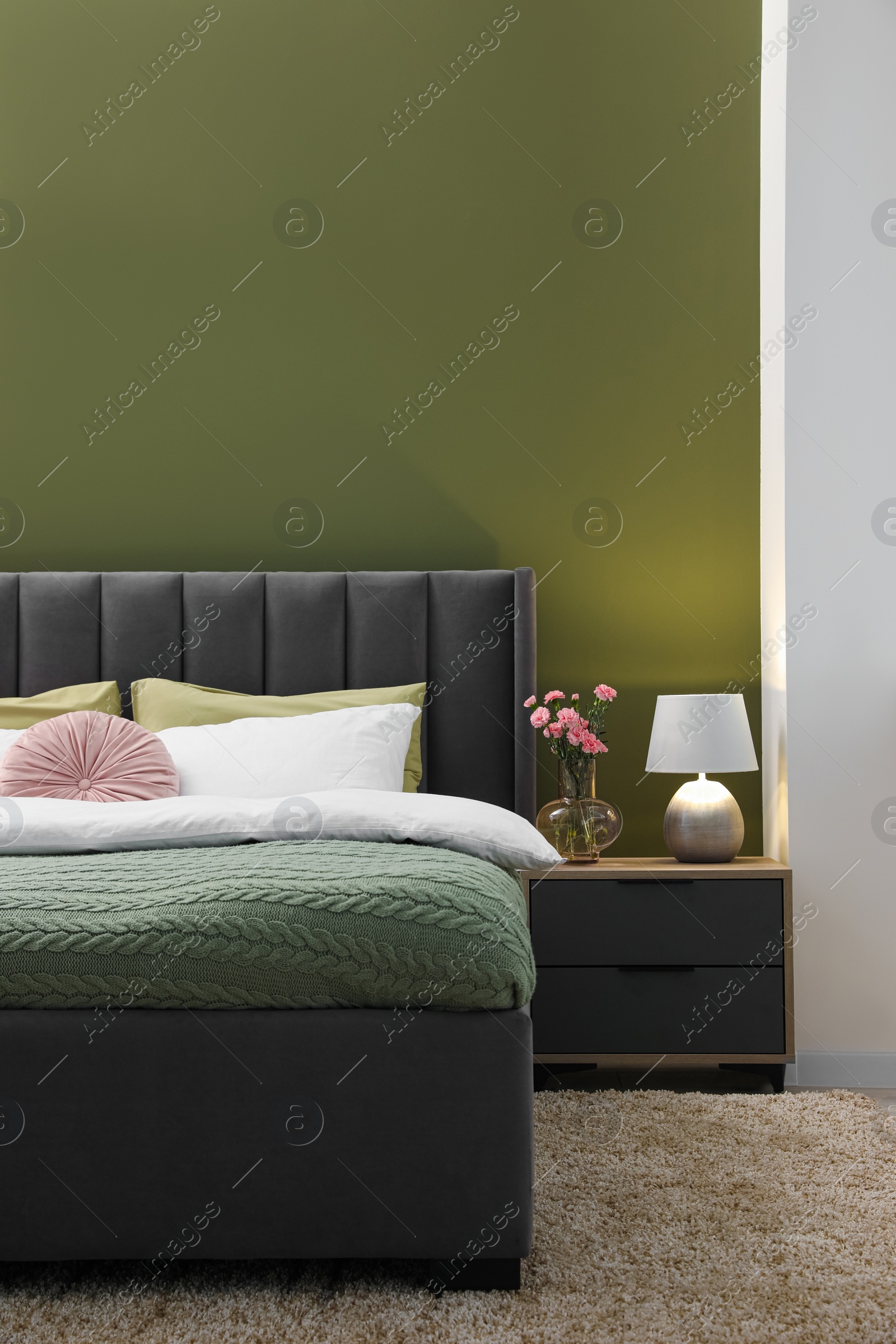 Photo of Large comfortable bed, nightstand, lamp and beautiful flowers in stylish room. Interior design