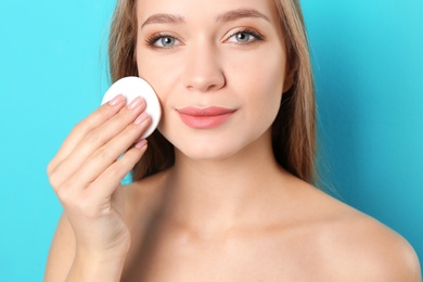 Photo of Portrait of beautiful young woman removing makeup with cotton pad on color background
