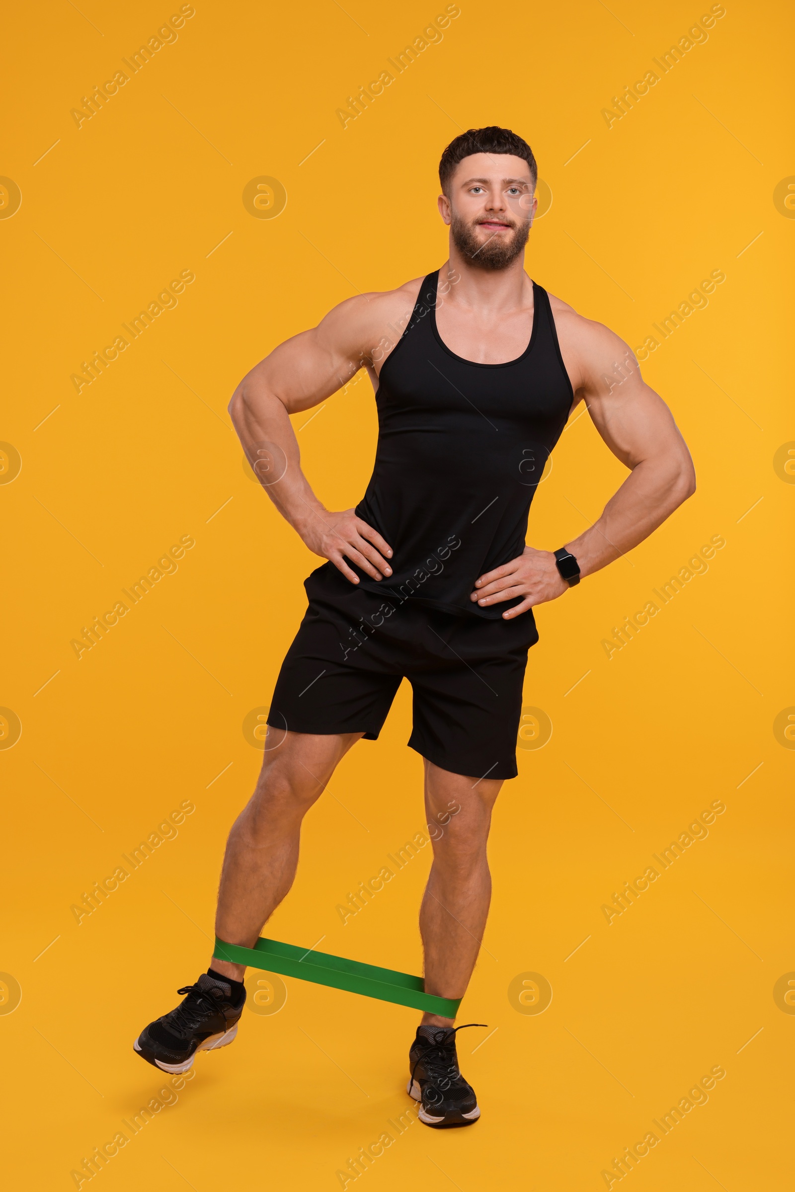 Photo of Young man exercising with elastic resistance band on orange background