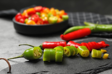 Photo of Slate plate with red and green cut chili peppers on grey table, closeup. Space for text