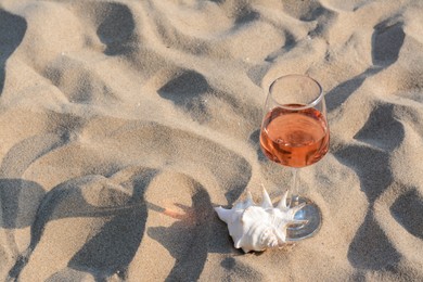 Photo of Glasstasty rose wine and seashell on sand, space for text