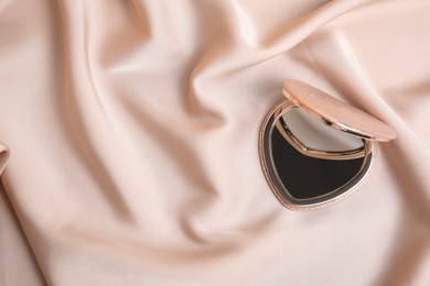 Photo of Stylish heart shaped cosmetic pocket mirror on rose gold fabric, top view. Space for text
