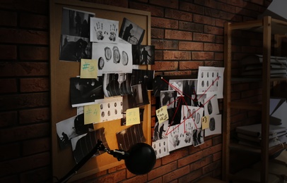 Photo of Boards with fingerprints, crime scene photos and red threads on brick wall. Detective agency
