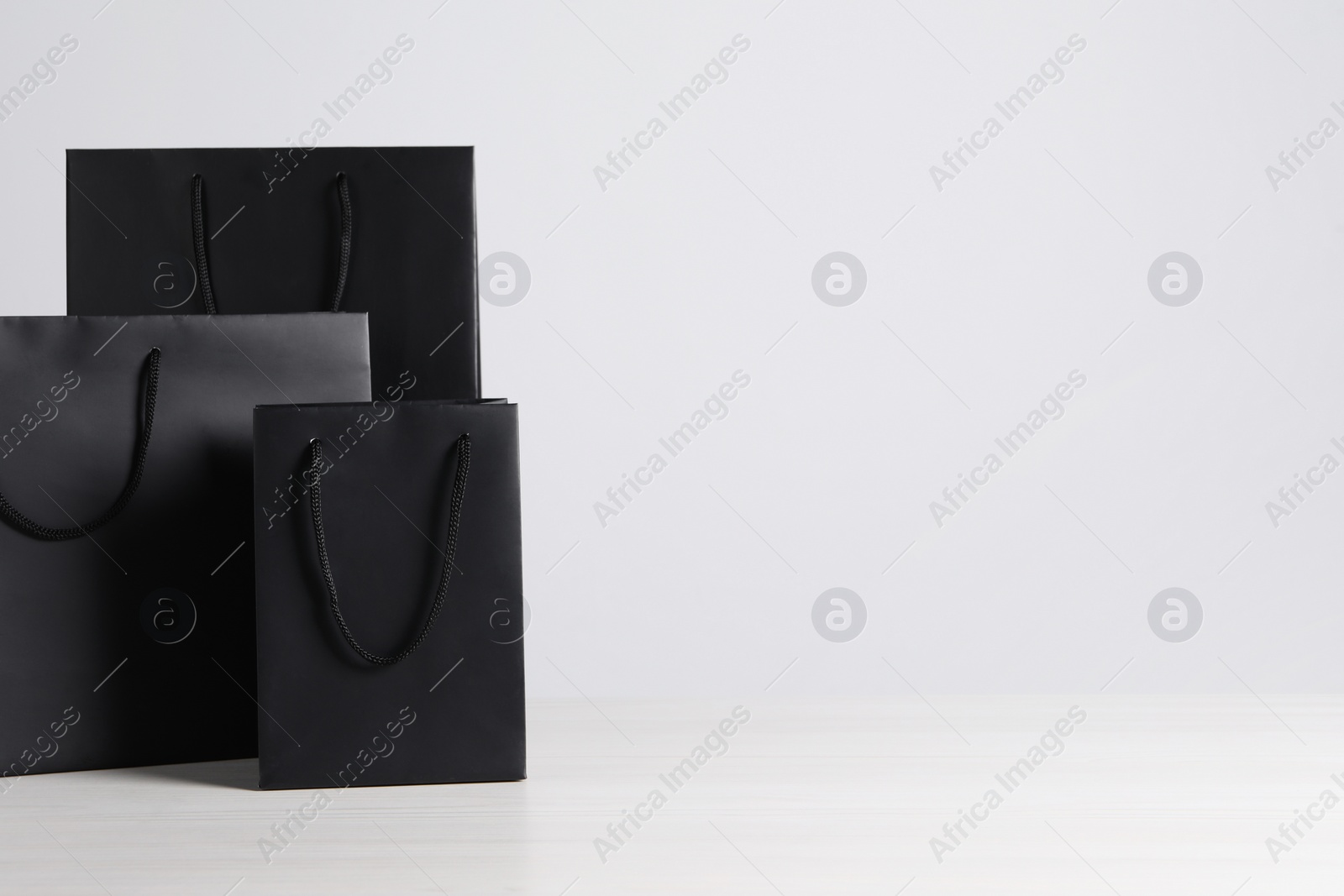 Photo of Black paper bags on white wooden table, space for text