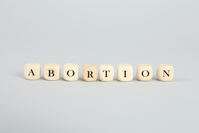 Photo of Word Abortion made of wooden cubes on light grey background