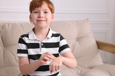 Little boy putting sticking plaster onto hand on sofa indoors. Space for text