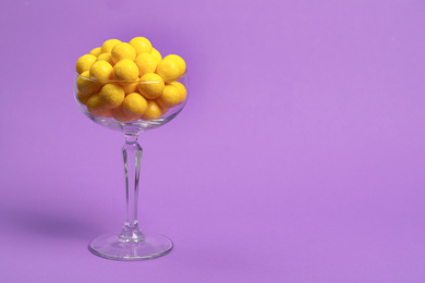 Photo of Tasty lemon chewing gums in glass on purple background. Space for text