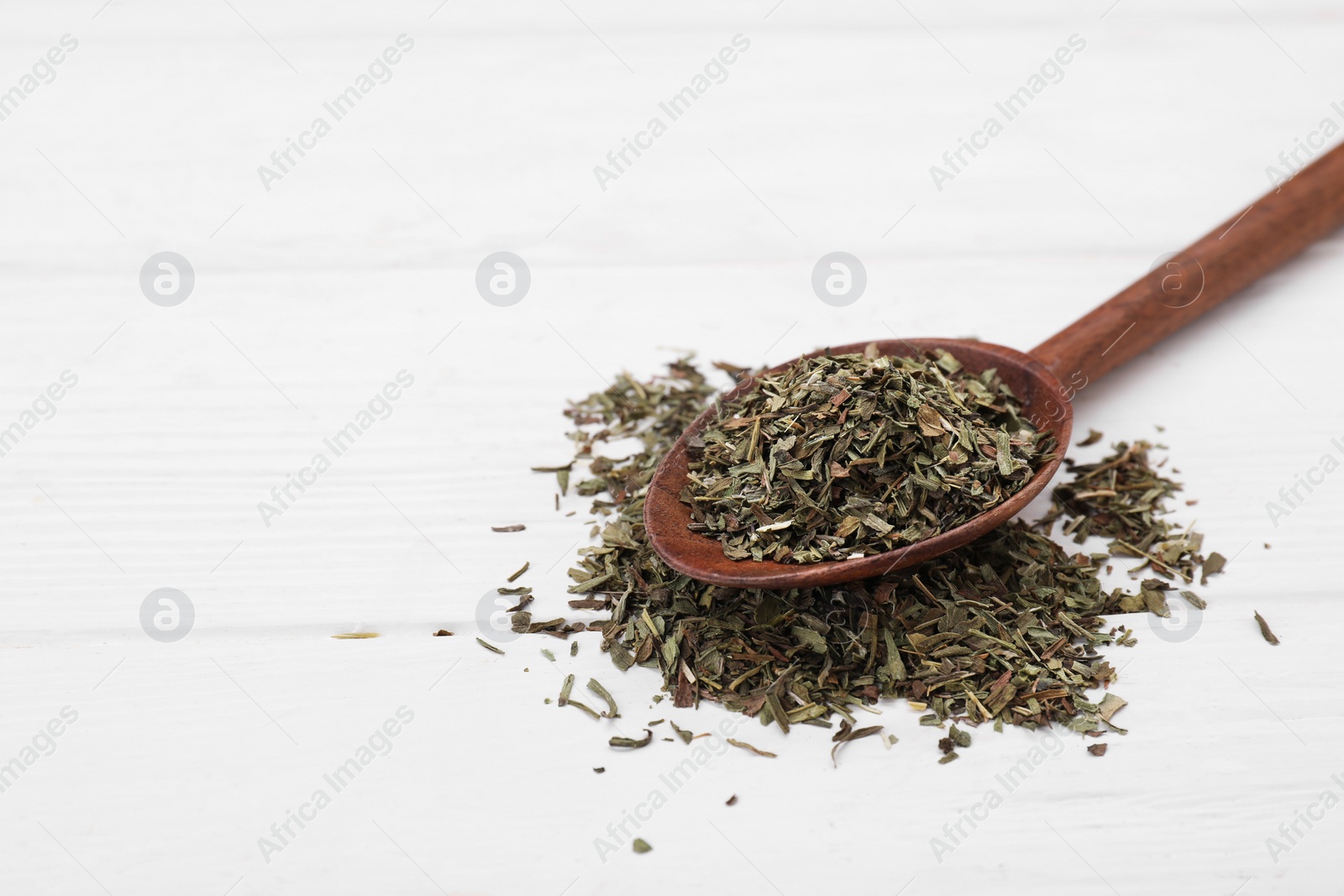 Photo of Spoon of dry tarragon on white wooden table. Space for text