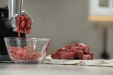 Photo of Electric meat grinder with beef mince on white table against blurred background, selective focus. Space for text