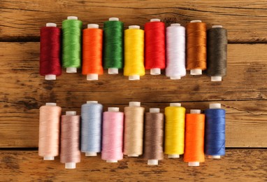 Photo of Different colorful sewing threads on wooden background, flat lay