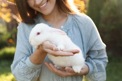 Happy woman holding cute rabbit outdoors on sunny day, closeup