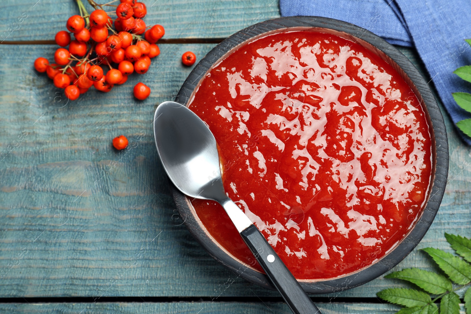 Photo of Delicious rowan jam on light blue wooden table, flat lay. Space for text