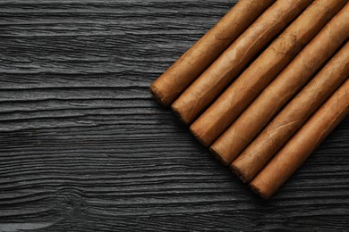 Many cigars on black wooden table, flat lay. Space for text