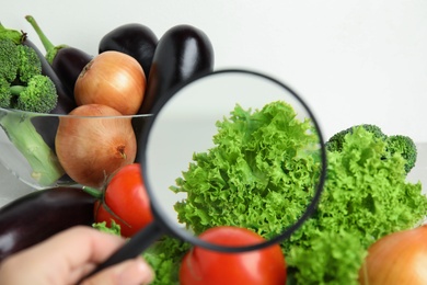Photo of Woman with magnifying glass exploring vegetables, closeup. Poison detection