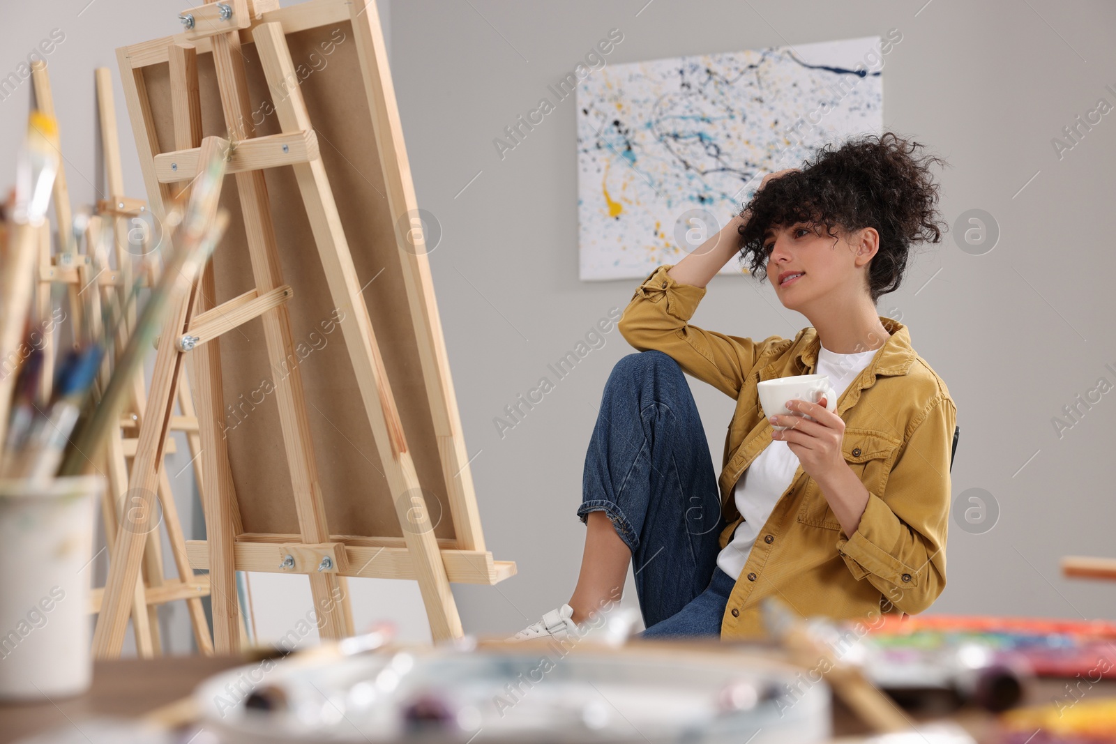 Photo of Young woman with cup near easel in studio