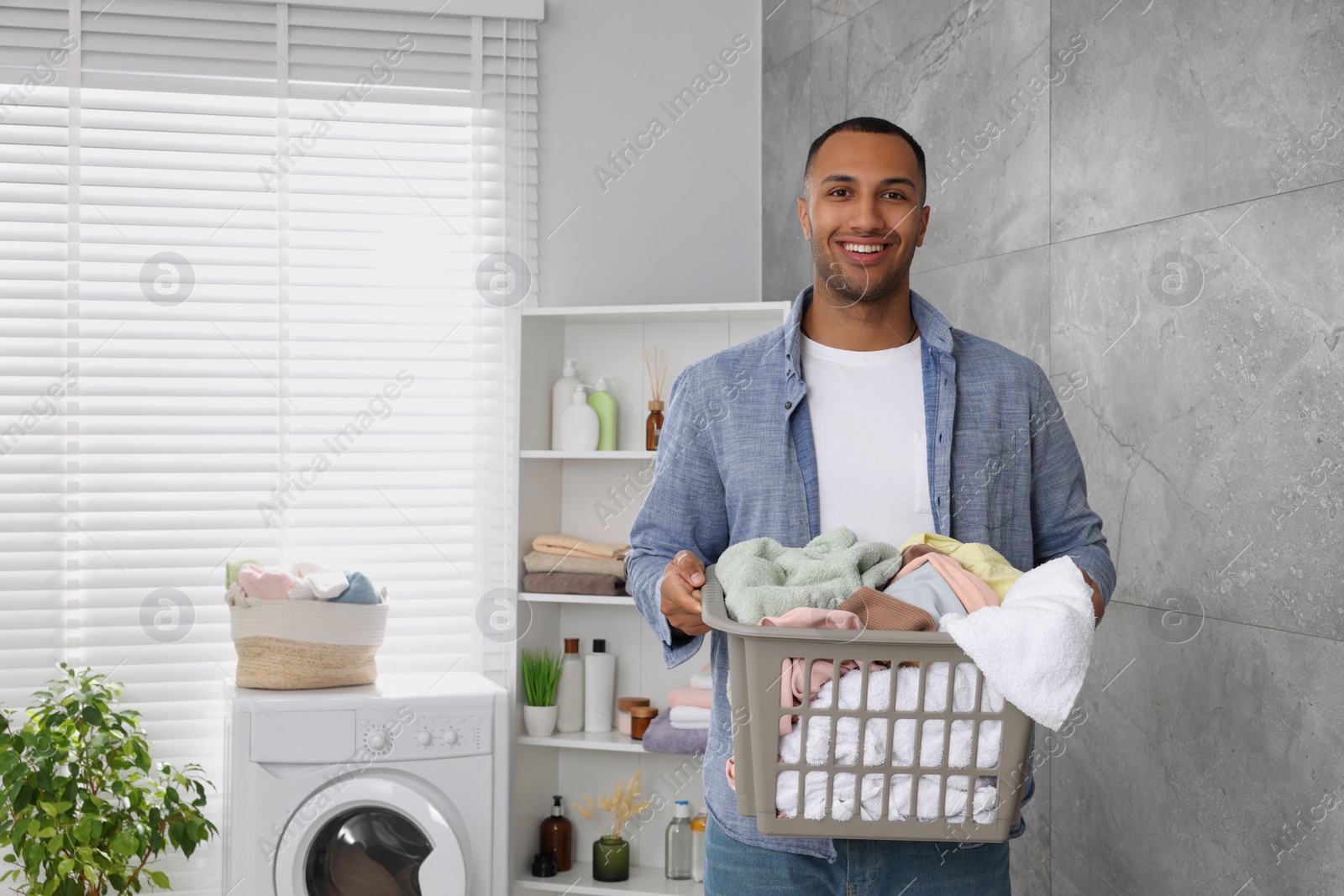 Photo of Happy man with basket full of laundry in bathroom. Space for text