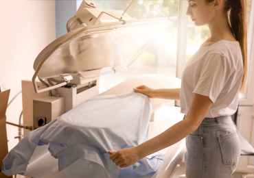 Woman using modern ironing press in dry-cleaning