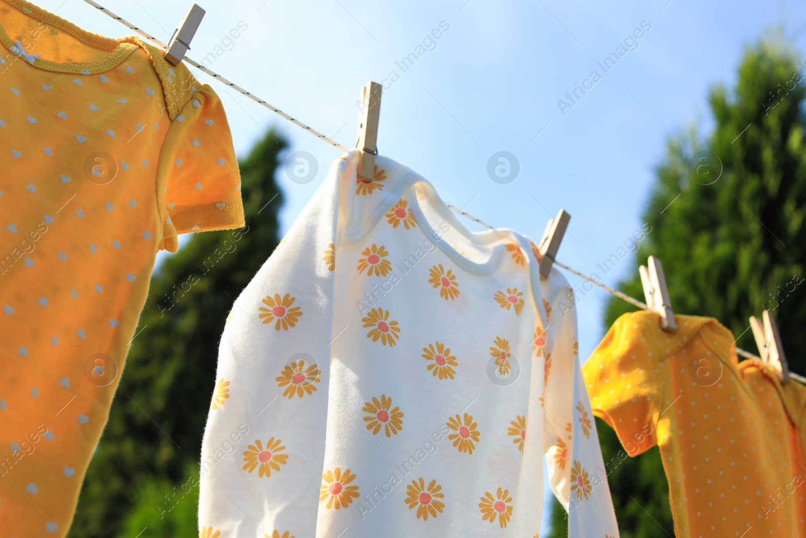 Photo of Clean baby onesies hanging on washing line in garden. Drying clothes