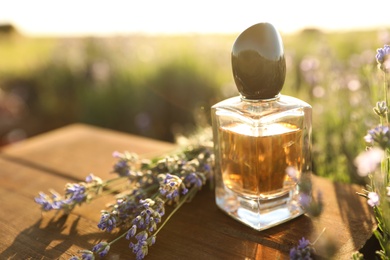 Photo of Bottle of luxury perfume and lavender flowers on wooden table in blooming field. Space for text