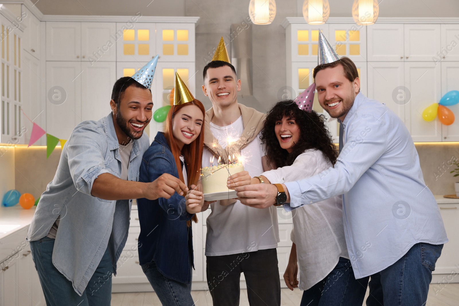 Photo of Happy friends with tasty cake and sparklers celebrating birthday in kitchen