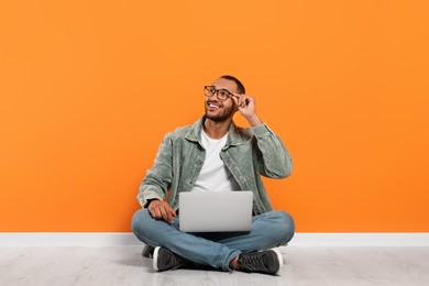Photo of Smiling young man with laptop sitting on floor near orange wall, space for text