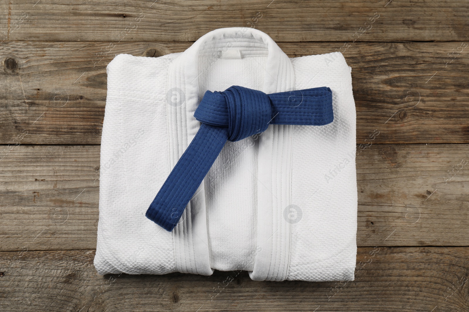 Photo of Blue karate belt and white kimono on wooden background, top view