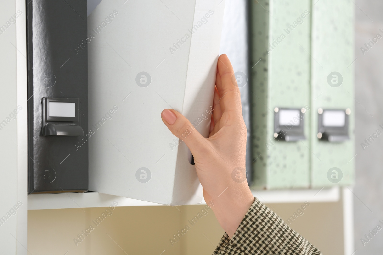 Photo of Woman taking folder with documents from shelf, closeup