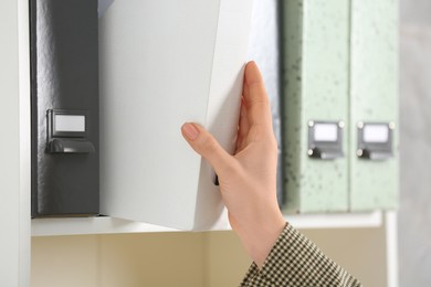 Photo of Woman taking folder with documents from shelf, closeup