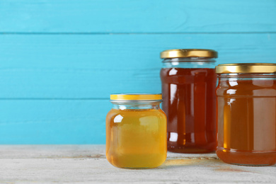 Jars with different types of organic honey on wooden table against light blue background. Space for text